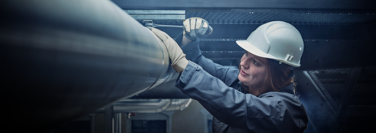 woman with helmet and wrench assembling a pipe coupling