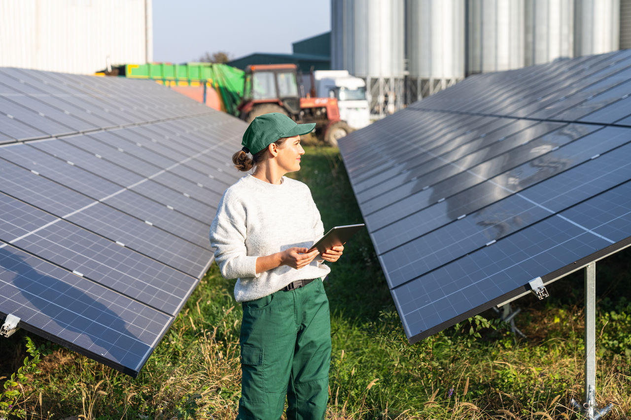 Female farmer with digital tablet on a modern farm using solar panels. Agricultural silos in the background	.